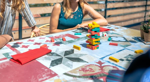 Preview: Jenga tower over table with unrecognizable people playing in a rooftop party