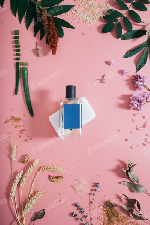 Preview: Perfume bottle in flowers on pink background. Spring background with aroma parfume. Flat lay