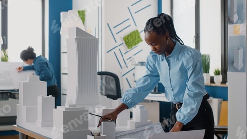 Preview: African american woman analyzing blueprints plan and building model to work on architecture