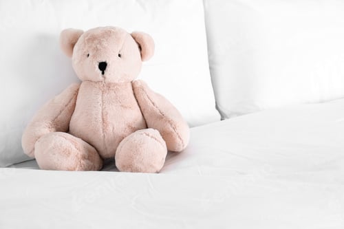 Preview: Cute teddy bear sitting on bed indoors. Space for text
