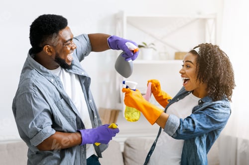 Preview: Cleaning Fun. Joyful African Couple Playfully Aiming With Sprayers At Each Other