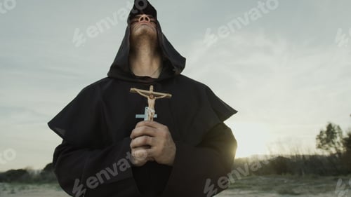 Preview: Religious Monk Prays With A Crucifix Of Jesus In His Hand Kneeling On The Sand