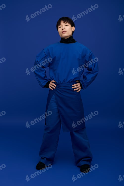 Preview: Stylish young asian man posing confidently in vibrant blue outfit against a solid backdrop
