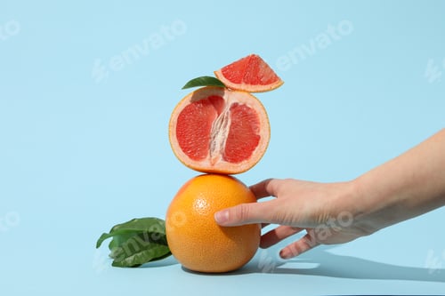 Preview: Sliced and whole grapefruit with leaves in female hand on blue background