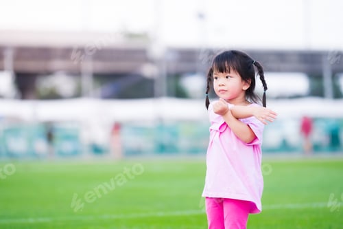 Preview: Cute Asian girl is exercising in the grass. Happy child is using both arms and twists the body.