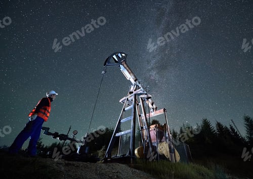 Preview: Engineer near pump jack at starry night.