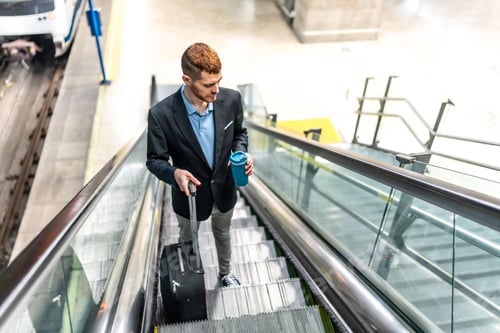 Preview: Businessman going down on escalator at station holding coffee and luggage