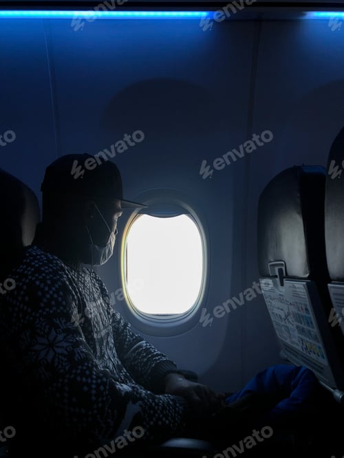 Preview: An African American man in a medical mask is flying in an airplane at the window of the porthole