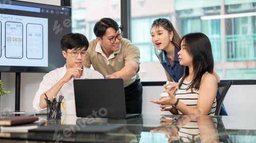 Preview: Asian man pointing and woman coworkers looking at laptop on glass top table in office's meeting room
