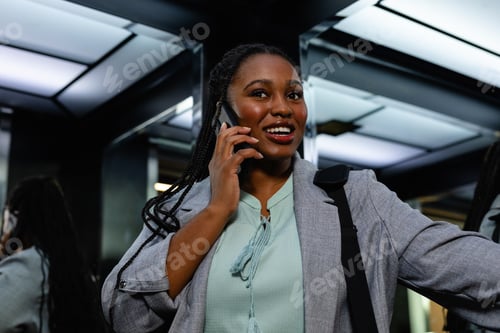 Preview: Happy plus size african american casual businesswoman talking on smartphone in elevator