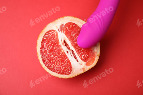 Preview: Half of grapefruit and purple vibrator on red background, flat lay. Sex concept