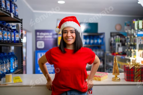 Preview: Young woman smiling, wearing santa hat and red shirt at retail store counter