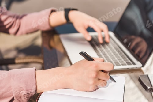 Preview: partial view of man remote working on laptop and making notes at tabletop