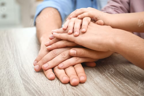 Preview: Happy family holding hands at wooden table indoors, closeup view