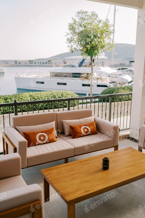 Preview: Beige sofas and armchairs with pillows stand near a wooden table on the terrace on the embankment