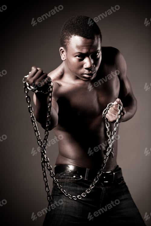 Preview: Young half naked african man standing and holding massive chains in hands