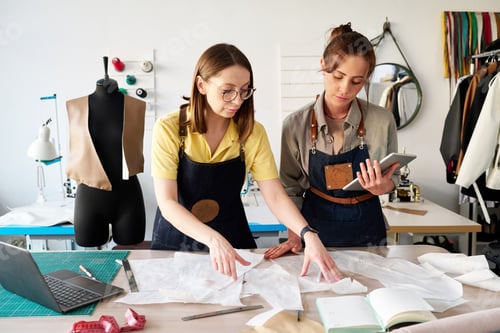 Preview: Two female tailors choosing sewing paper patterns by workplace in studio