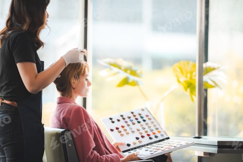 Preview: Young woman in robe and casual selecting hair color from catalogue in modern salon