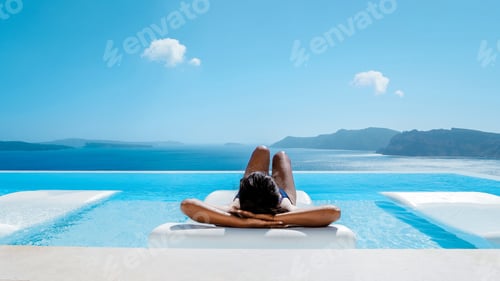 Preview: Young multicultural Asian woman in Infinity pool looking out over the ocean of Oia Santorini Greece