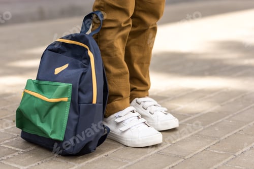 Preview: cropped shot of stylish schoolboy standing with backpack on street