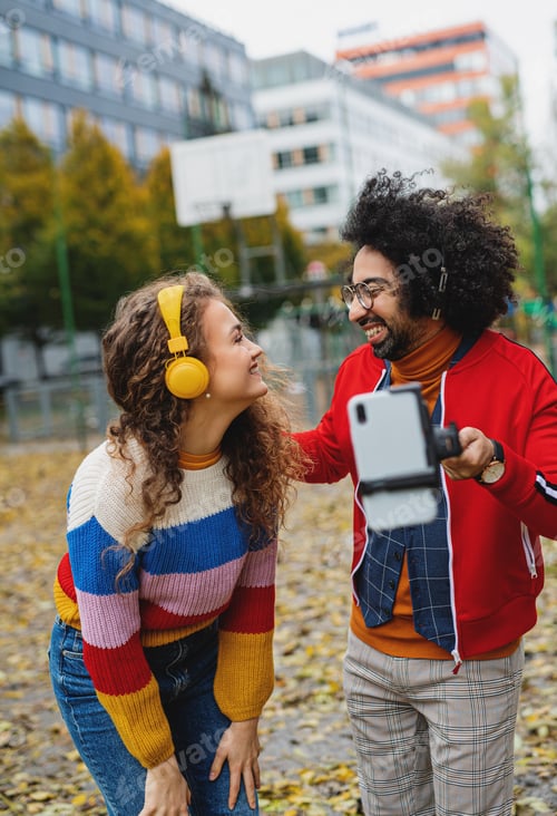 Preview: Young couple with smartphone making video for social media outdoors in park.
