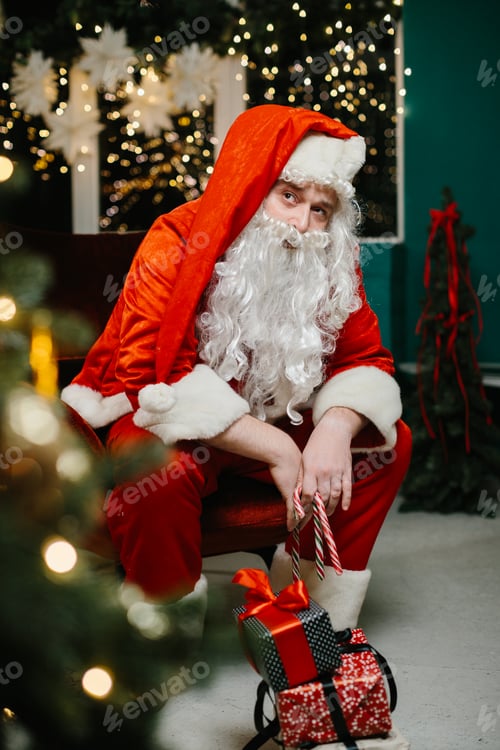 Preview: Santa claus holding candy canes sitting next to christmas gifts