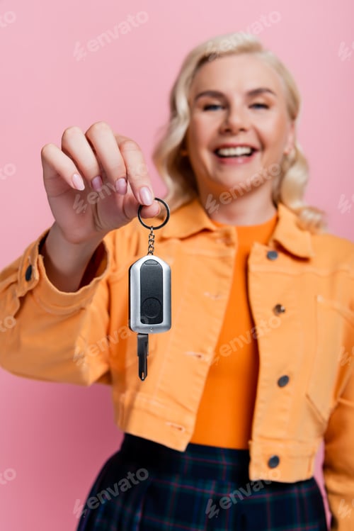 Preview: Car key in hand of blurred smiling driver isolated on pink