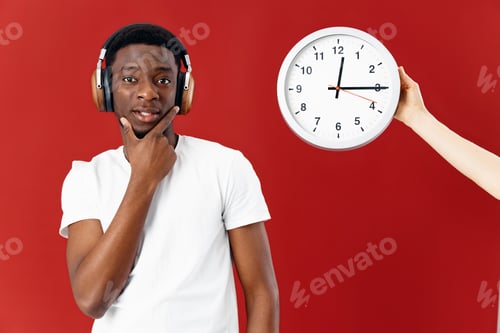 Preview: man of african appearance in headphones next to clock in white t-shirt cropped view