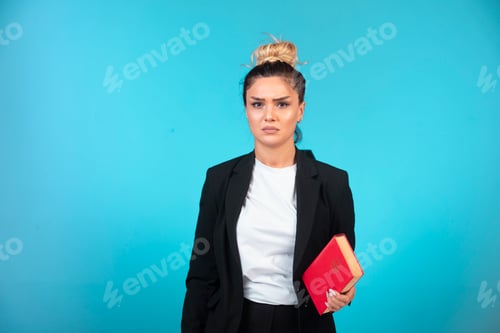 Preview: Young businesswoman in black blazer holding a book and looks depressed