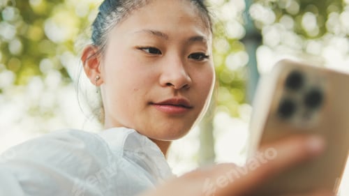 Preview: Close-up of young woman sitting on bench and using mobile phone