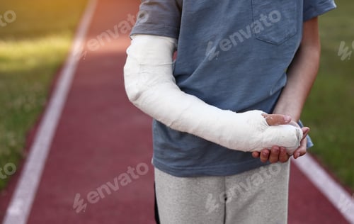 Preview: cropped photo of little boy with broken hand outdoors on sports ground on summer day. 9 years