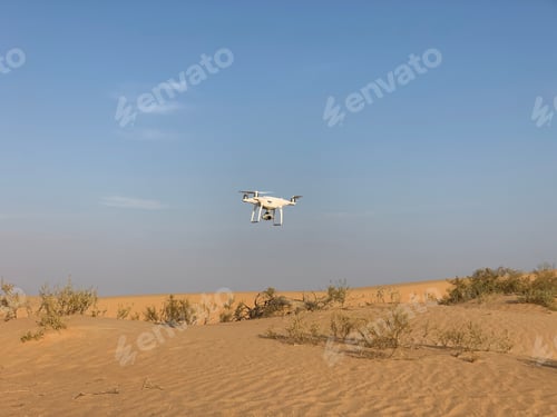 Preview: White Drone flying over low over the sand dunes and desert bushes of Dubai, taking pictures