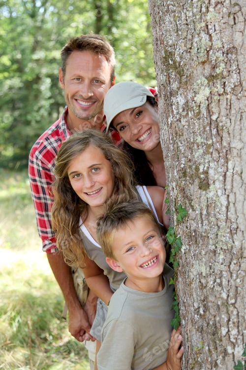 Vista previa: Smiling Family Standing Behind A Tree