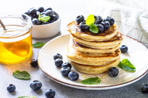 Preview: Pancakes with fresh blueberries and honey at white table.
