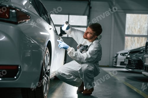 Preview: Searching for imperfections. Garage worker is holding lighting and checking surface of the car
