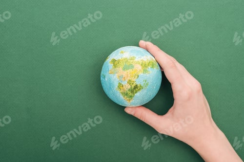 Preview: partial view of woman holding toy earth on green background with copy space