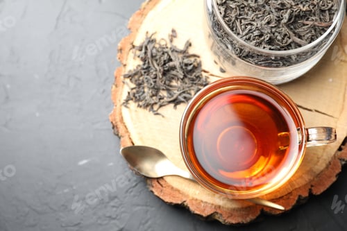 Preview: Aromatic black tea in cup and dry leaves on grey table, top view. Space for text