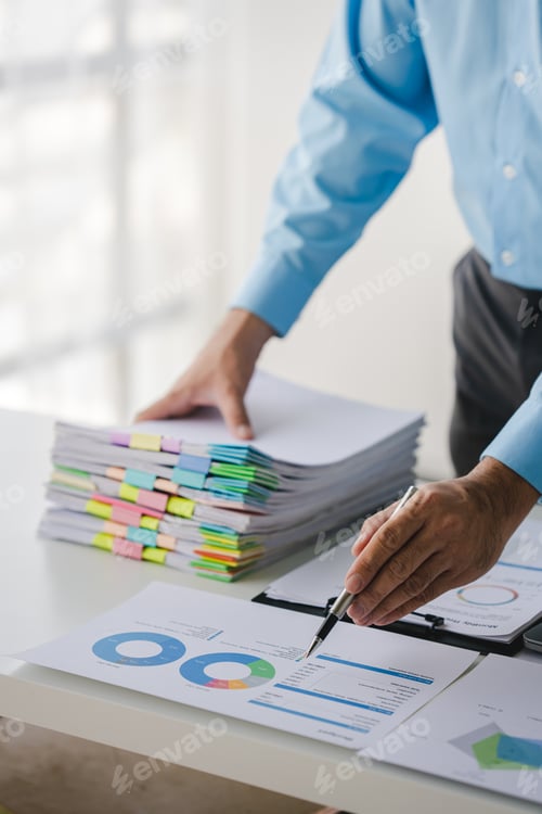 Preview: Businessman working on stacks of documents to search for information and check documents on office d