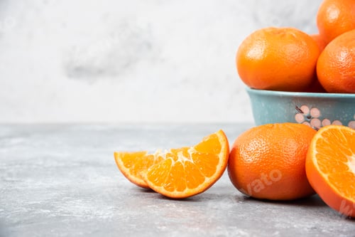 Preview: Whole and slice juicy fresh orange fruits in a bowl placed on a stone background