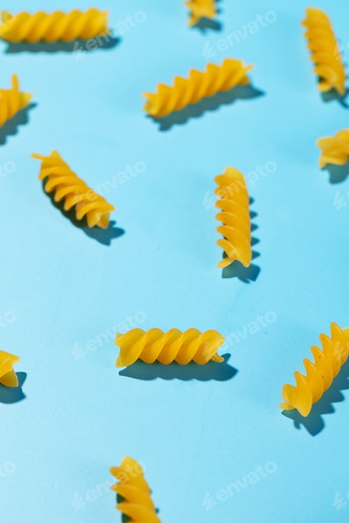 Preview: Uncooked fusilli pasta spirals scattered on a blue background in a decorative pattern