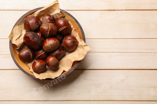 Preview: Roasted edible sweet chestnuts in bowl on wooden table, top view. Space for text
