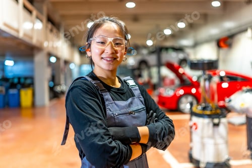 Preview: Young female mechanic smiling with crossed arms in car repair shop