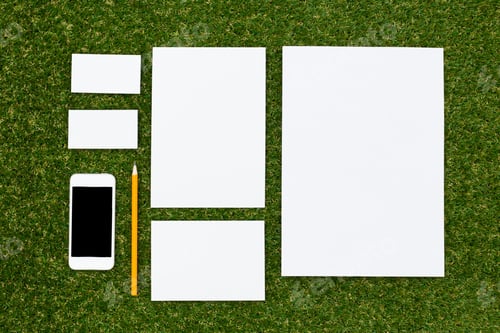 Preview: Various sizes of blank paper and a smartphone arranged on green grass for creative planning and