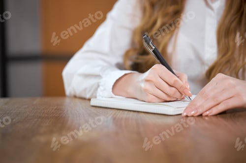 Preview: Woman Writes in Notebook at Wooden Desk