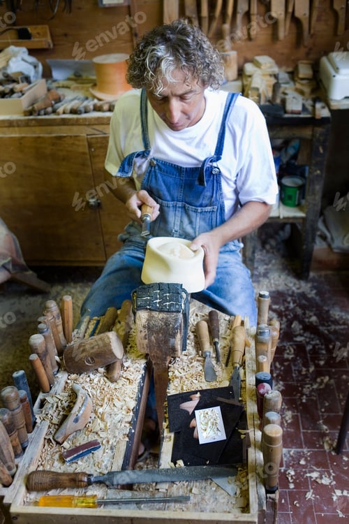 Preview: Carpenter using chisel on wooden mould for headwear in workshop