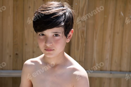 Preview: A contemplative boy in natural light with a wooden fence background