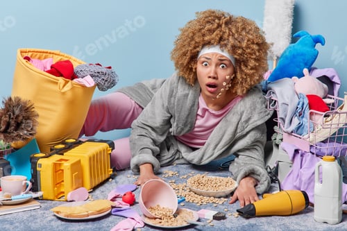 Preview: Amazed curly haired woman wears headband domestic robe stares with omg expression lies on floor with