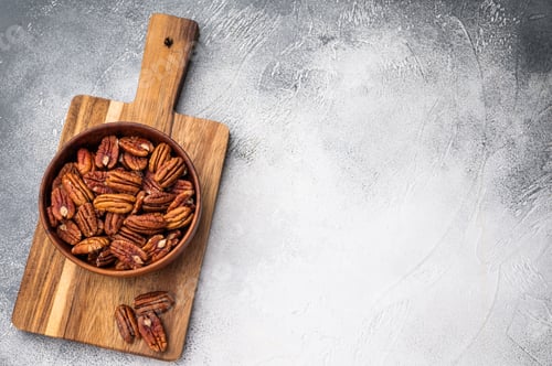 Preview: A top view of raw pecan halves in a wooden bowl against a bright white surface