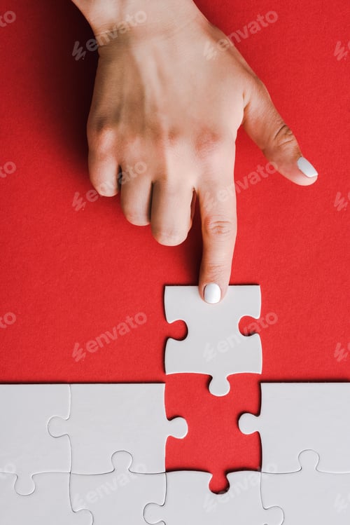 Preview: top view of woman pointing with finger at jigsaw near connected white puzzle pieces on red