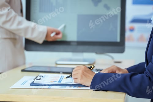 Preview: Two young Asian businesswomen sit at a table, engaged in a meeting.examine graphs and discuss